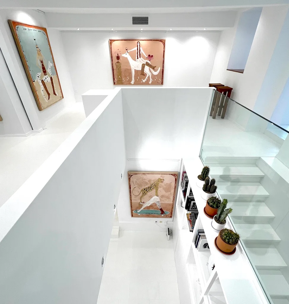 Overhead view of JAGAL's hang: the works spread across two levels, the glass staircase, the plants.