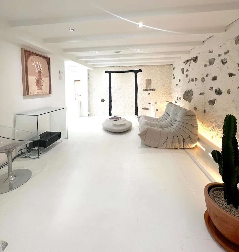 JAGAL's living room: a sofa facing a stone wall, a work on the wall, a coffee table. You sit down, you look, you talk.